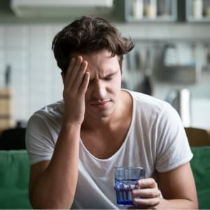 A man using EFT tapping to find easy relief from headaches while sitting on a couch holding a glass of water.